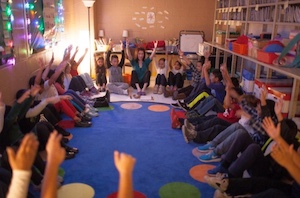 children sitting in circle raising arms